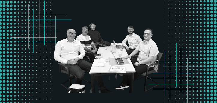 Group of five people seated around a meeting table with laptops, papers, and drinks, set against a dark background with teal dotted patterns